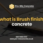 A low-angle, dark image of a person applying a brush finish to wet concrete using a wide push broom. The overlaid text asks, "what is Brush finish concrete".