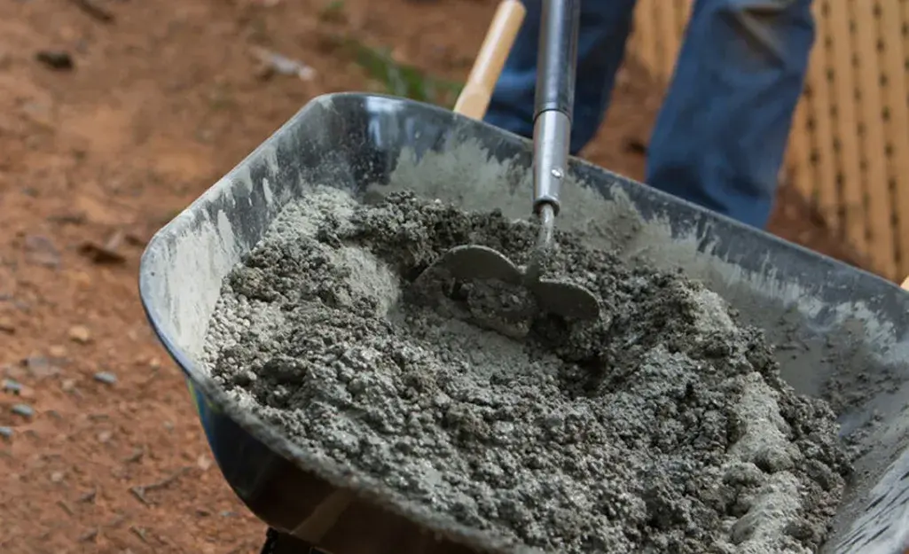A person is using a hoe to mix concrete in a wheelbarrow.